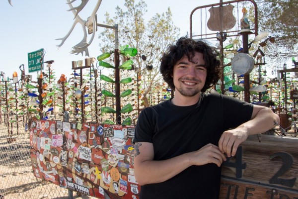 Harry Warnarr is leaning against a wooden partition with Bottle Tree Ranch behind him, featuring bottles of many colors. 
