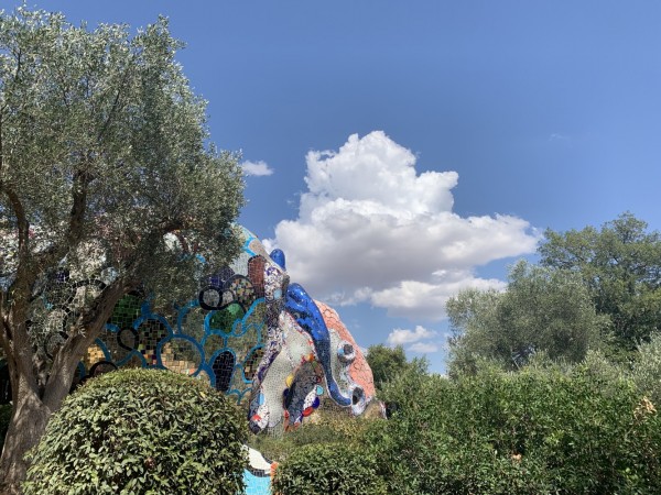Colorful sculptures emerge from trees with a blue sky and clouds above